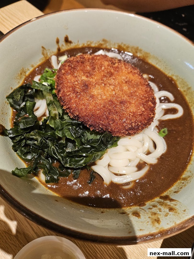 A bowl of udon noodles in curry broth with a fried cutlet and seaweed.