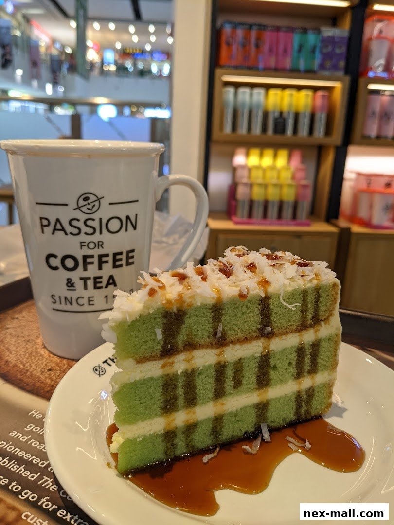 A slice of green layered cake with white frosting and caramel sauce is served with a mug.