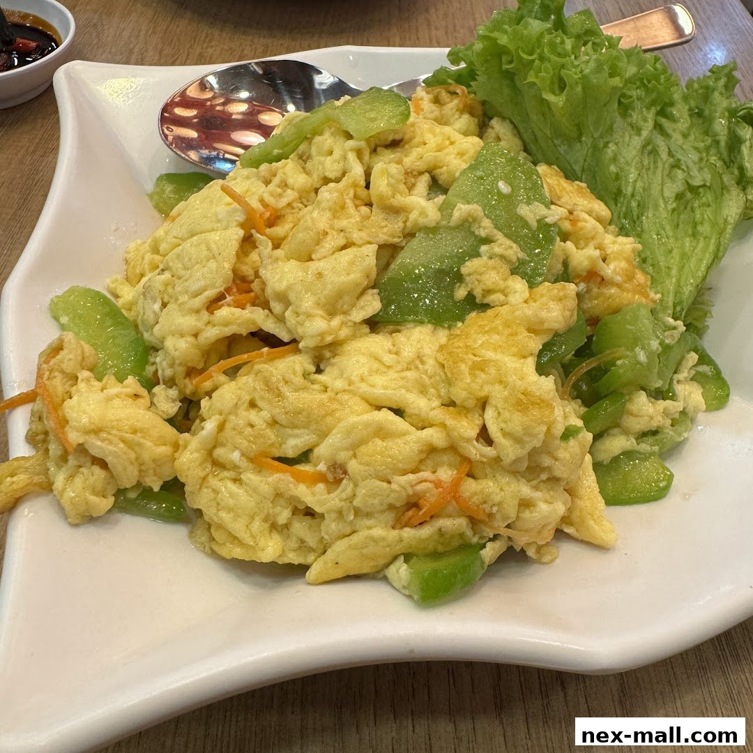 A plate of scrambled eggs with vegetables and lettuce garnish, served with a side of dipping sauce.