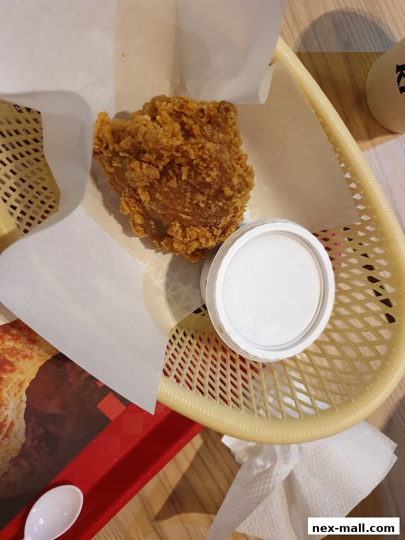 A close-up of a piece of crispy fried chicken in a basket with a small dipping sauce container.