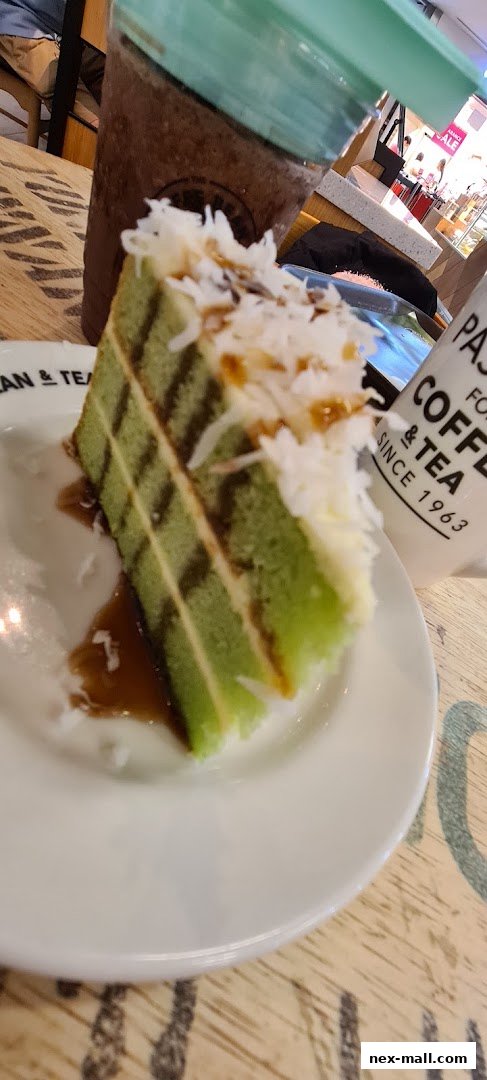 A slice of green layered cake with white frosting and coconut flakes on a white plate.