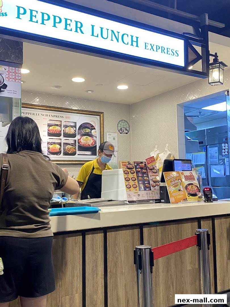 A customer orders at the Pepper Lunch Express counter with a staff member serving.