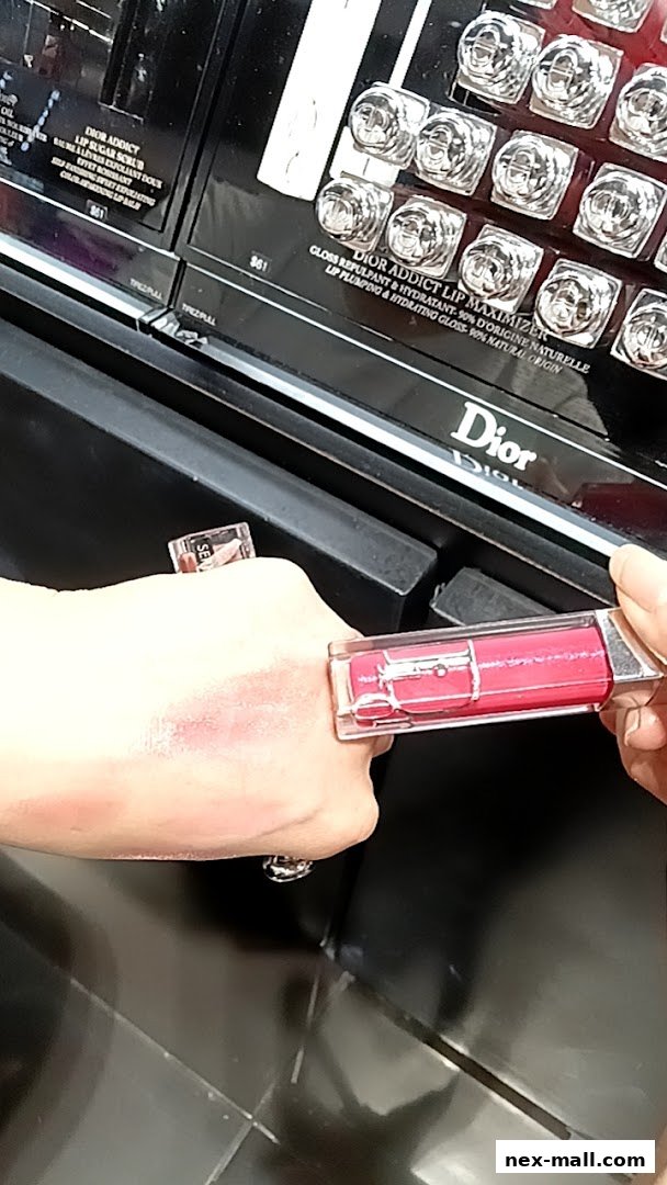 A hand is testing a Dior Addict Lip Maximizer gloss on the back of the hand.