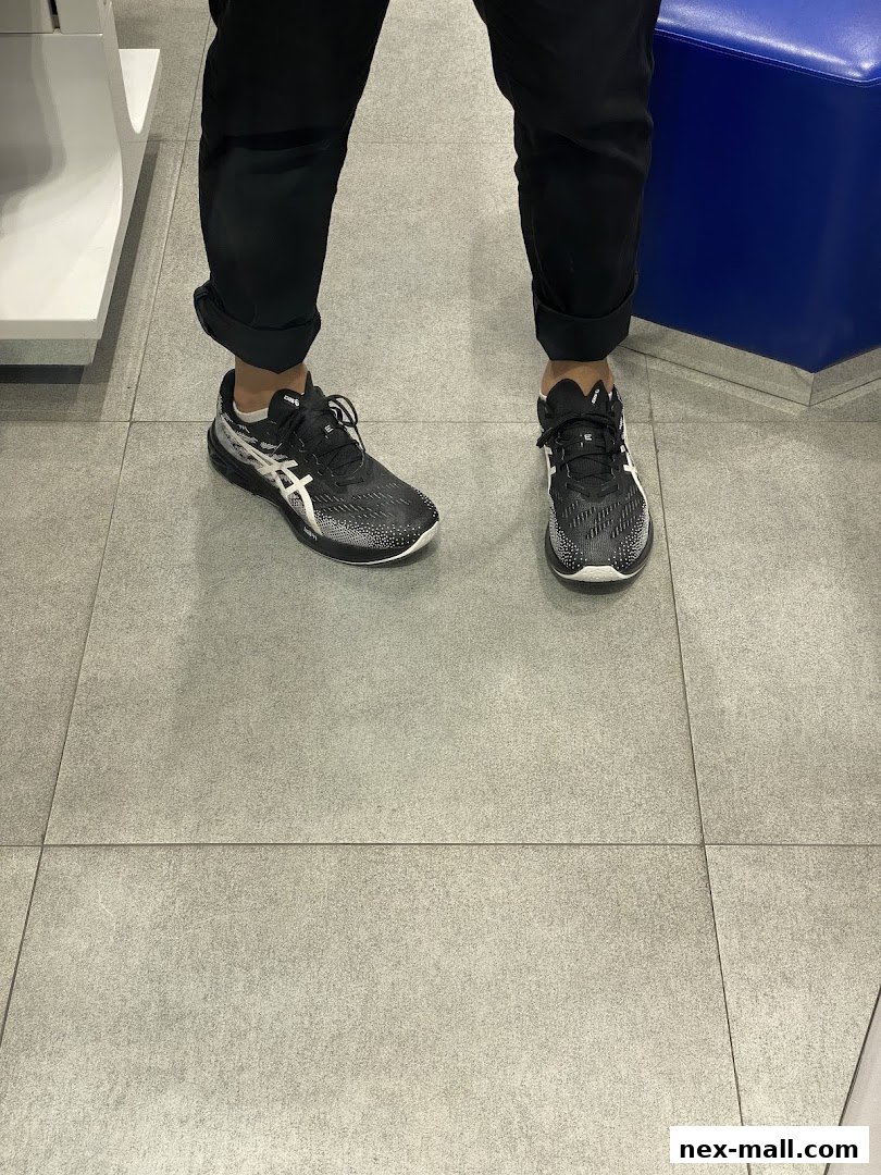 A person wearing black ASICS running shoes inside a store.