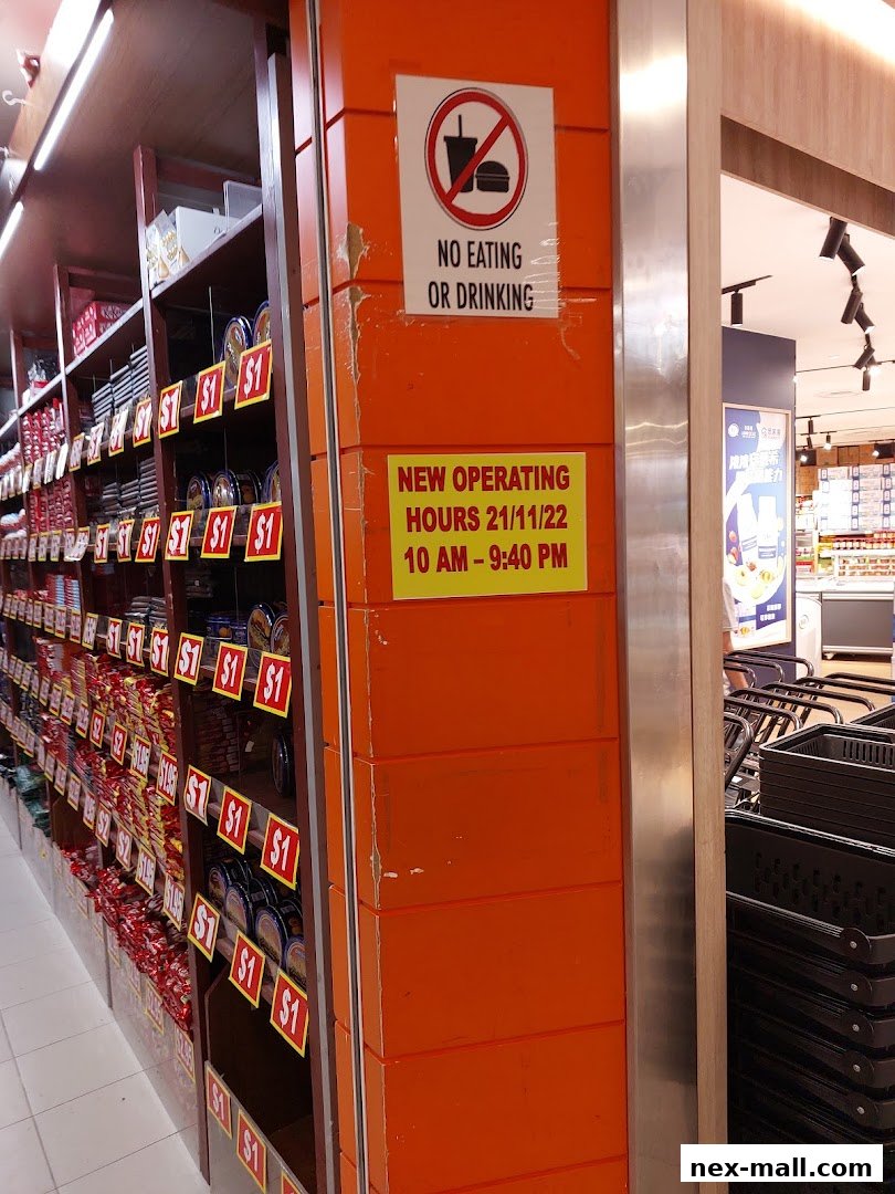 A retail store aisle with shelves stocked with products and signage indicating operating hours and no eating or drinking.