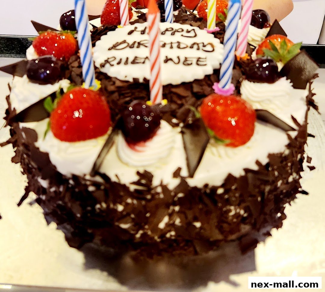 A decorated chocolate cake with strawberries, cherries, and birthday candles.