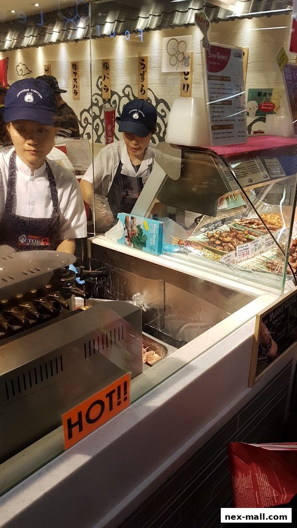Two staff members in uniform behind a counter displaying various skewers and food items.