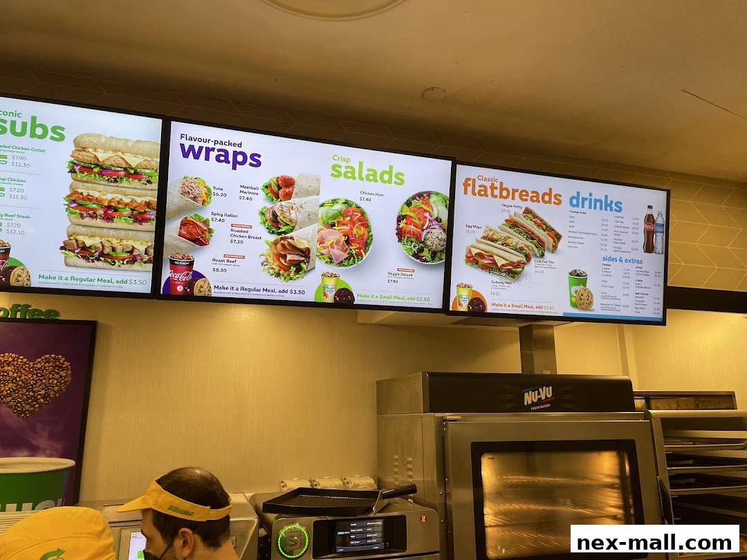 A digital menu board displaying various subs, wraps, salads, flatbreads, and drinks at Subway.