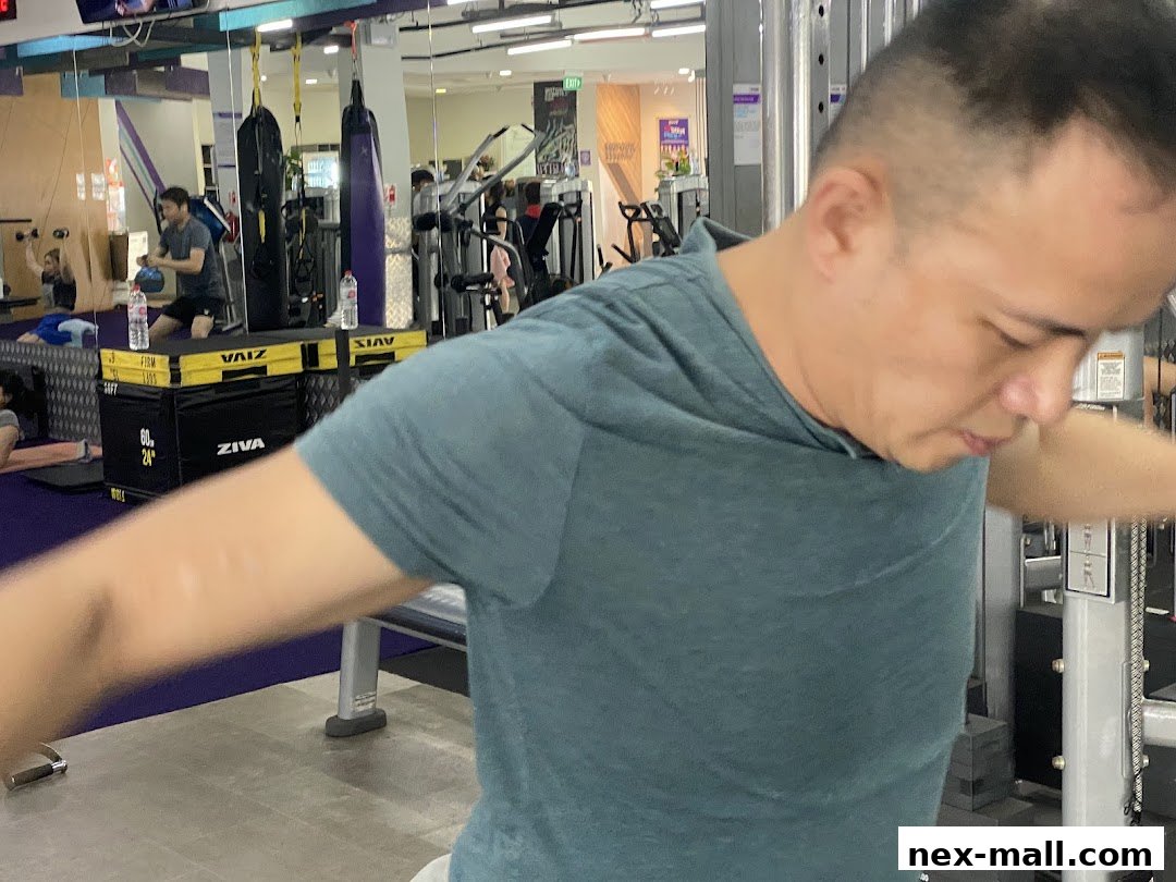 A man is working out on a cable machine in a gym with other people exercising.