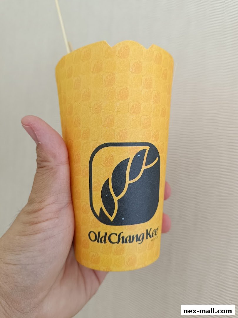 A hand holds a yellow paper cup with the Old Chang Kee logo and a patterned design.