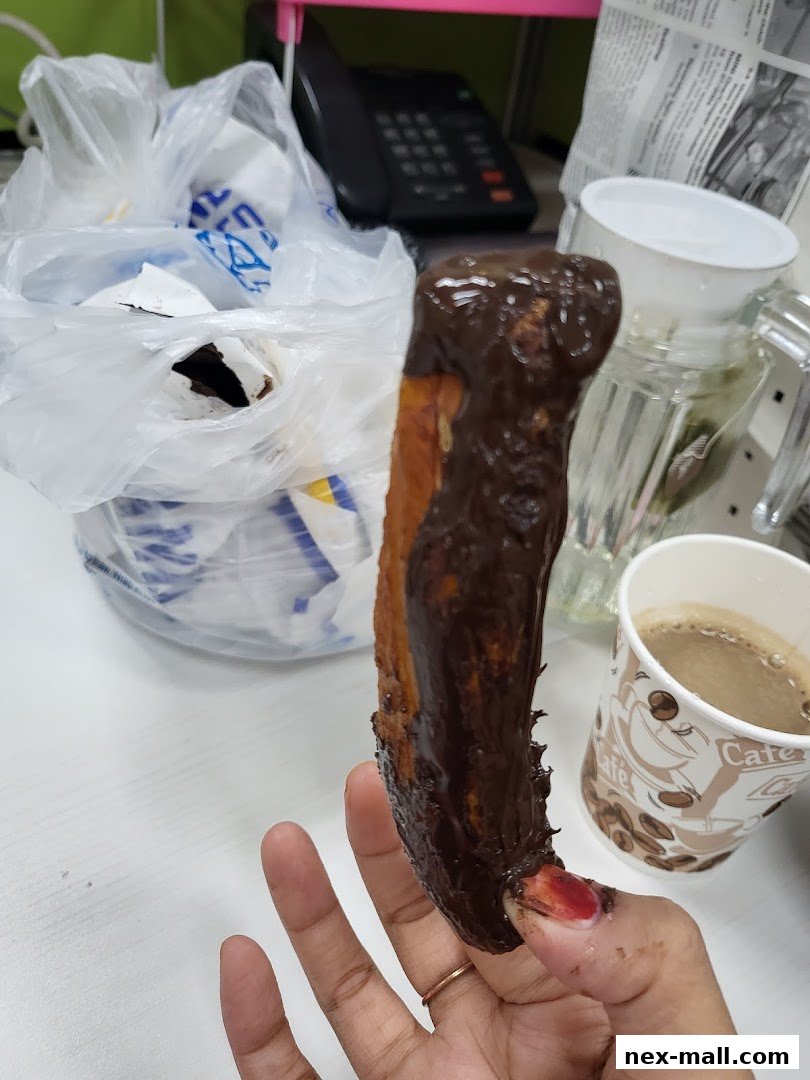 A hand holds a chocolate-dipped pretzel next to a cup of coffee.