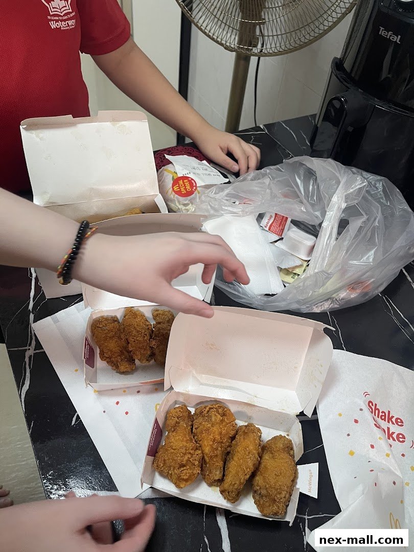 Several boxes of fried chicken wings and a burger from McDonald's are laid out on a table.