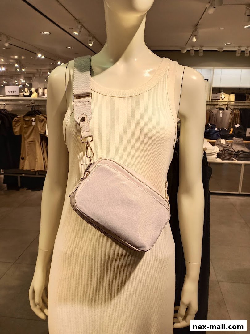 A mannequin displays a light-colored dress and a crossbody bag in a retail store.