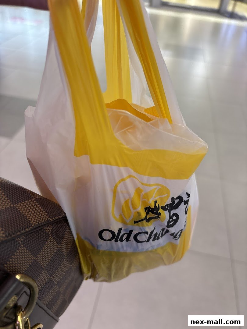 A person holding a white and yellow Old Chang Kee shopping bag with food inside.