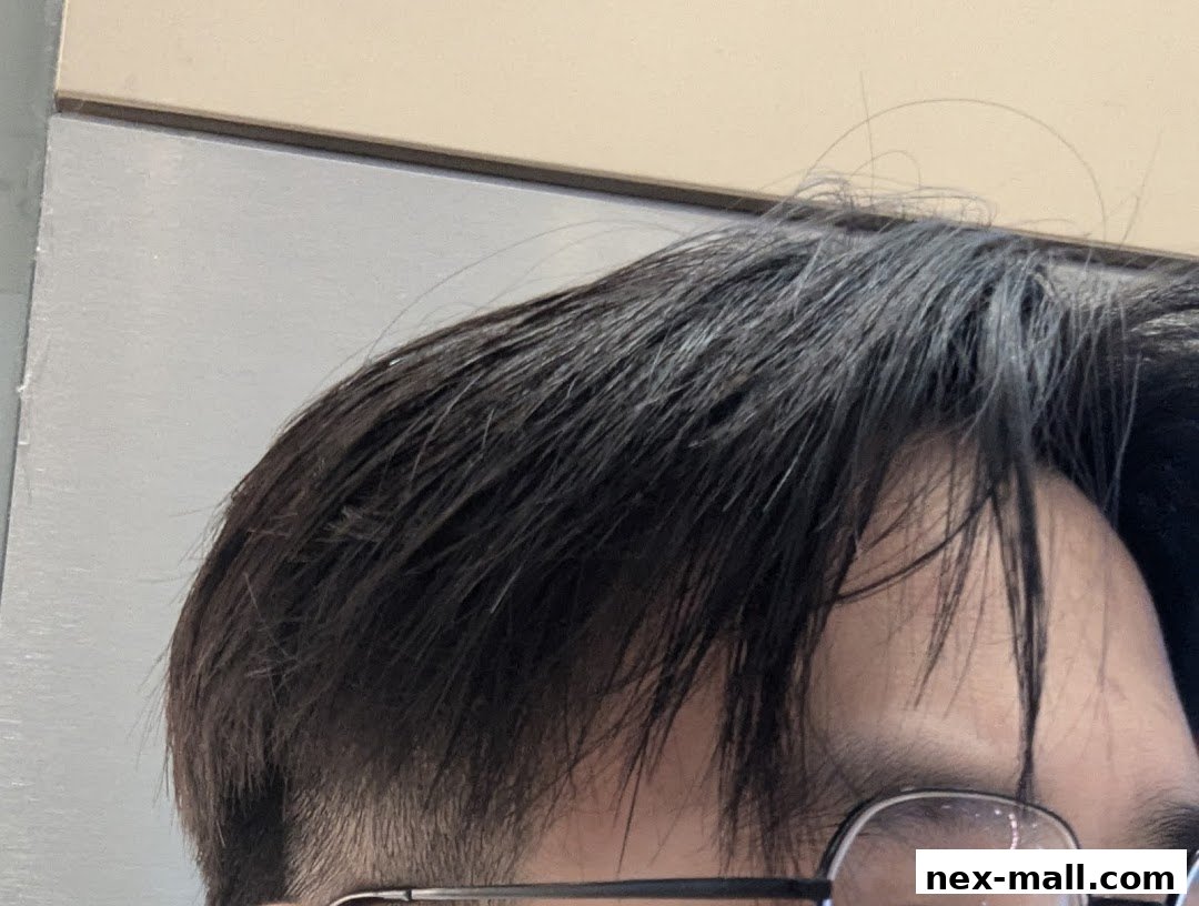 Close-up of a person's dark hair and glasses, with a neutral background.