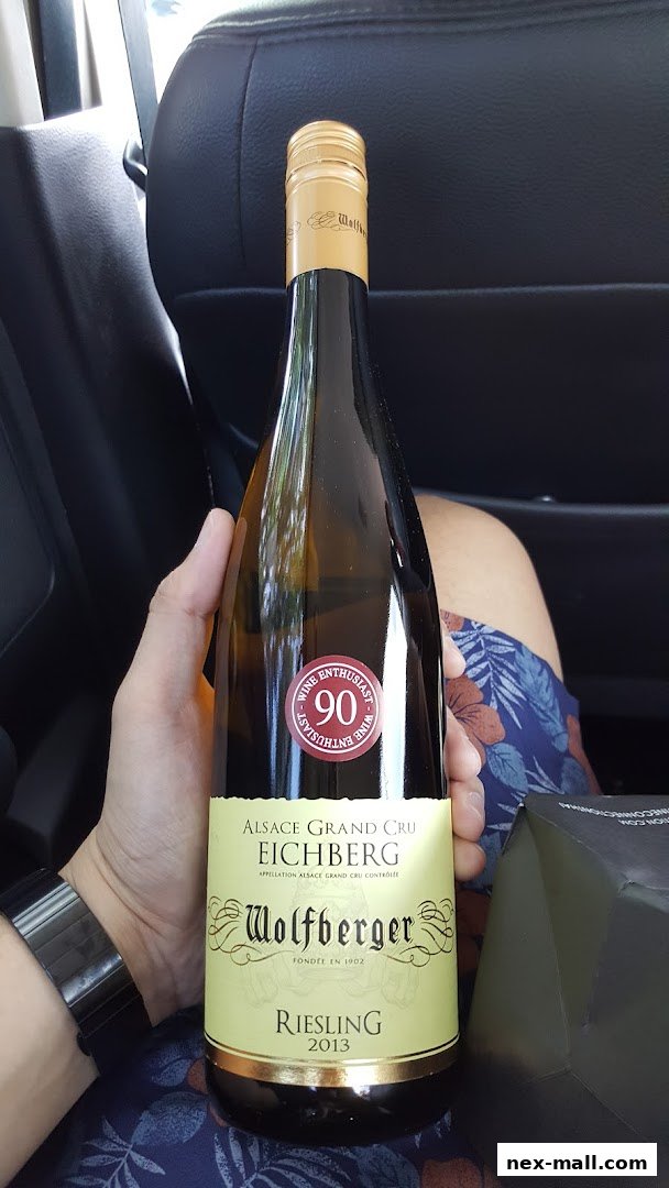 A hand holds a bottle of Wolfberger Riesling 2013 wine with a '90 Wine Enthusiast' sticker.