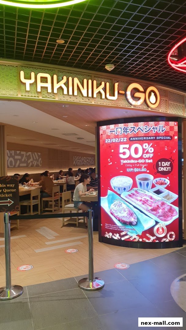 The entrance of Yakiniku-GO NEX, featuring a large digital display advertising a 50% off anniversary special.