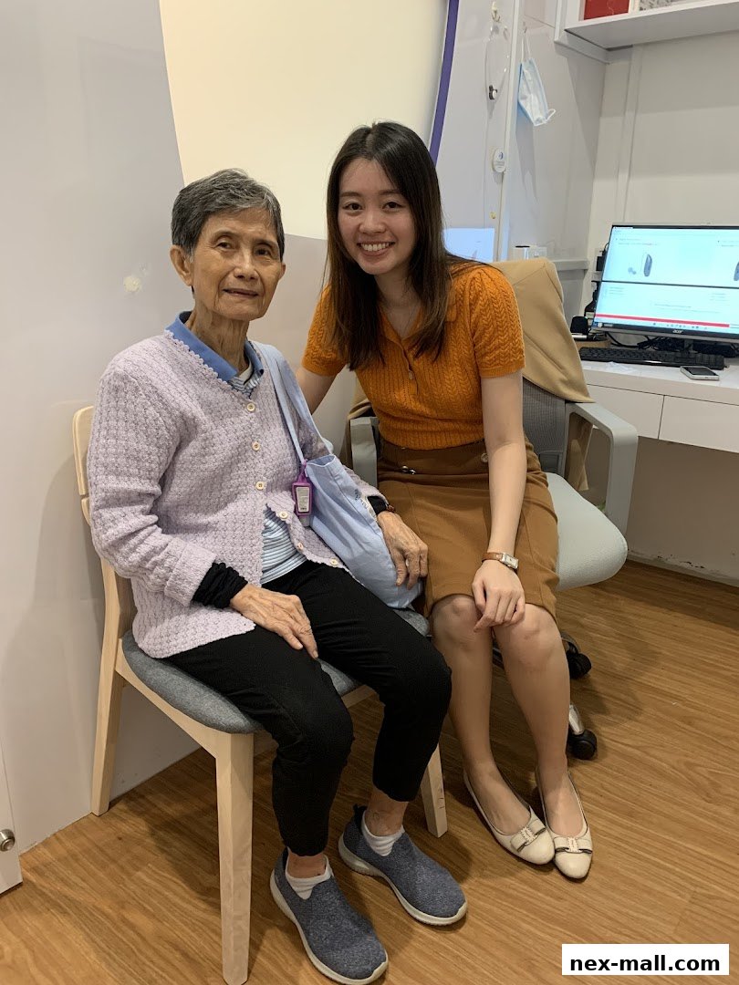 A young woman smiles next to an elderly woman seated in a hearing clinic.