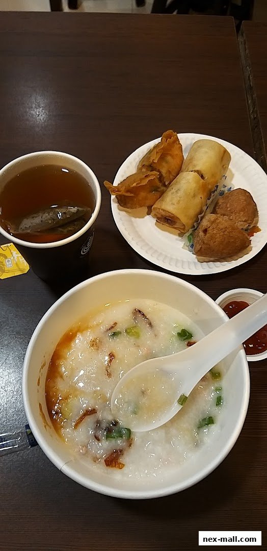 A bowl of congee with spring rolls, dumplings, and a cup of tea.