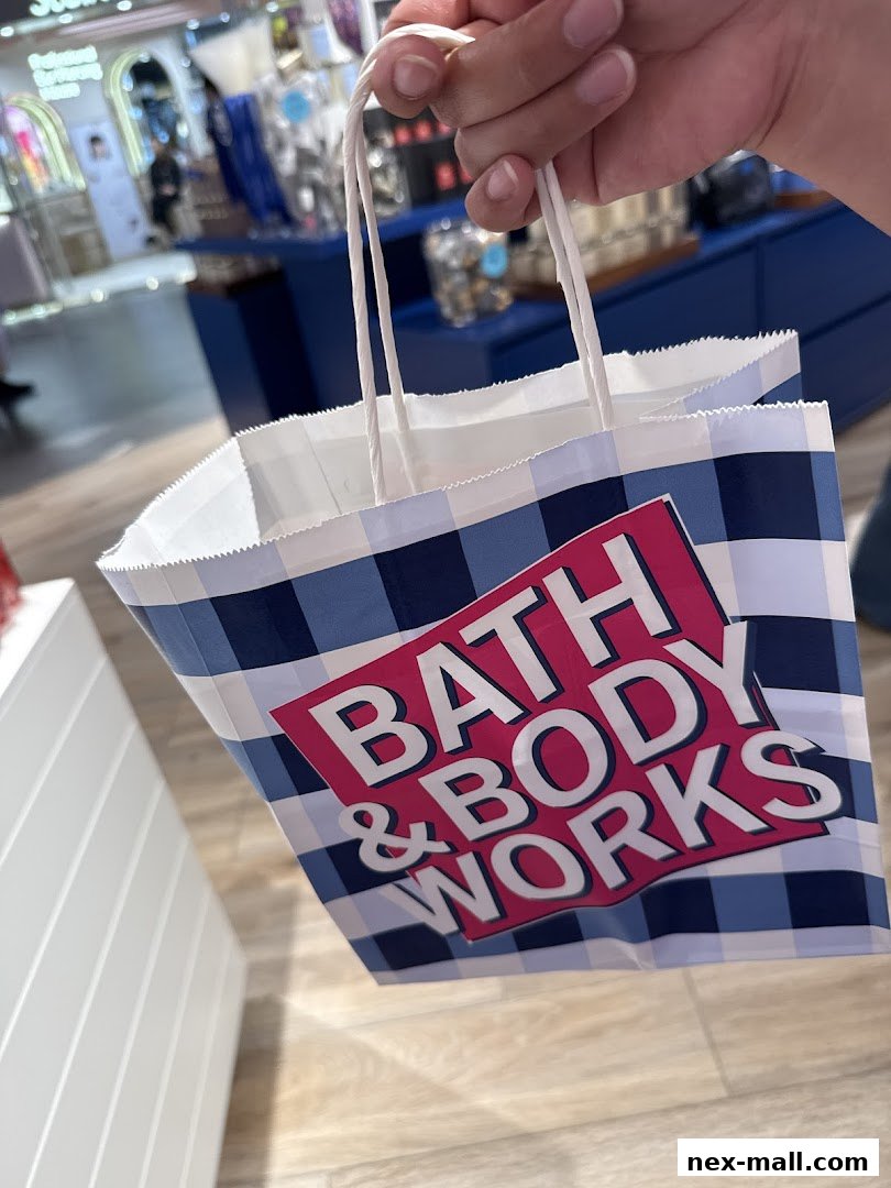 A hand holds a Bath & Body Works shopping bag inside a store.