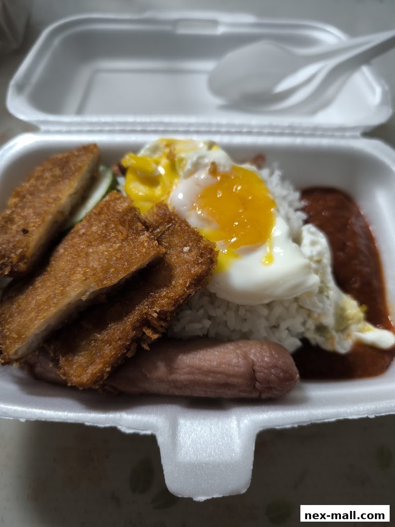 A takeaway container filled with rice, fried chicken, a fried egg, sausage, and sambal.