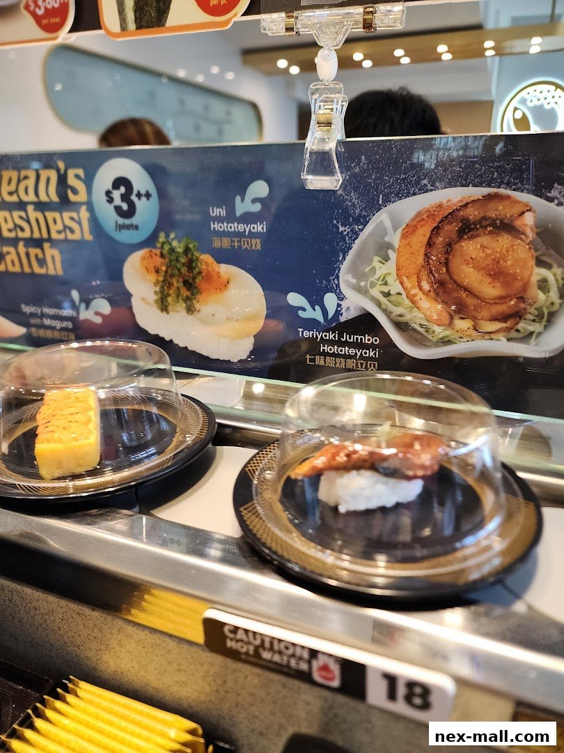 A conveyor belt sushi restaurant display featuring Uni Hotateyaki and Teriyaki Jumbo Hotateyaki.