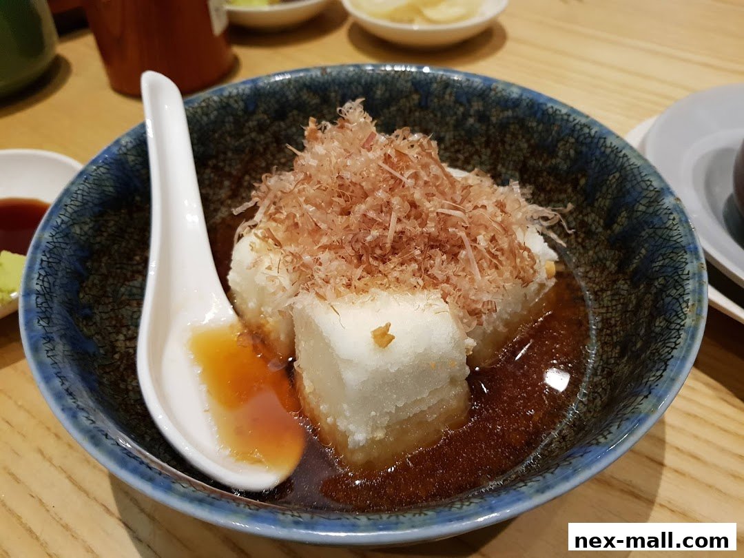 A close-up of a Japanese dish with tofu, broth, and bonito flakes, served with a spoon.