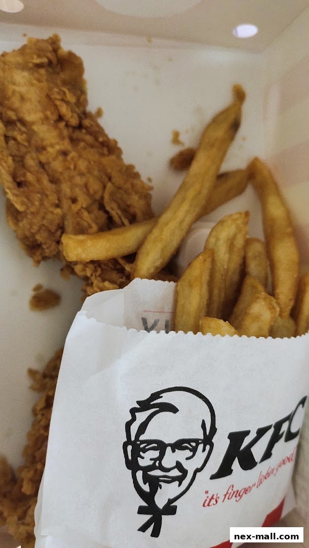 A close-up of KFC fried chicken and fries in a white paper bag.