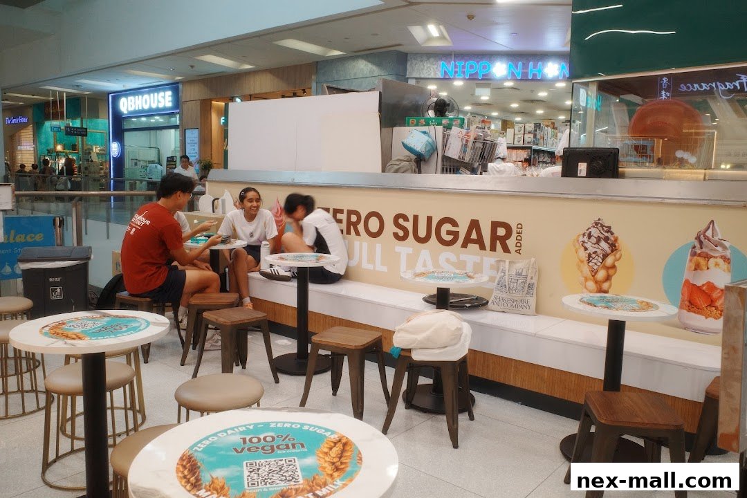 People sitting at tables in front of a dessert shop with "Zero Sugar Full Taste" signage.