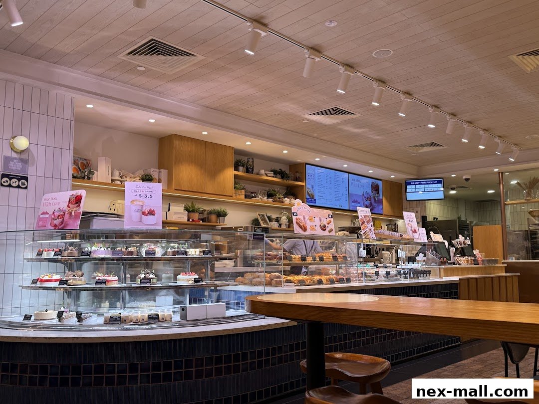 Interior view of Paris Baguette NEX showcasing a display of cakes and pastries, with a digital menu board.