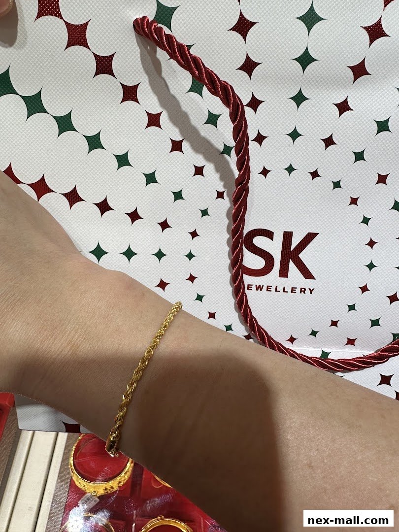 A person's arm wearing a gold bracelet with a SK Jewellery bag in the background.