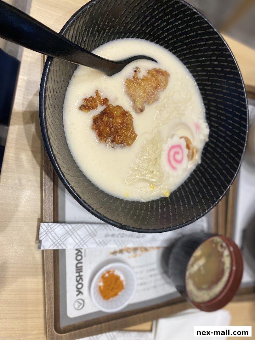 A bowl of creamy ramen with fried chicken pieces and narutomaki fish cake.