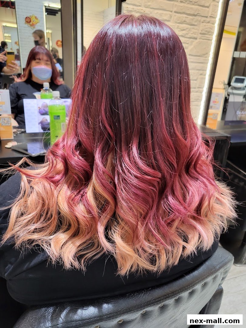 A person with vibrant, multi-toned red and blonde ombre hair styled in loose waves.