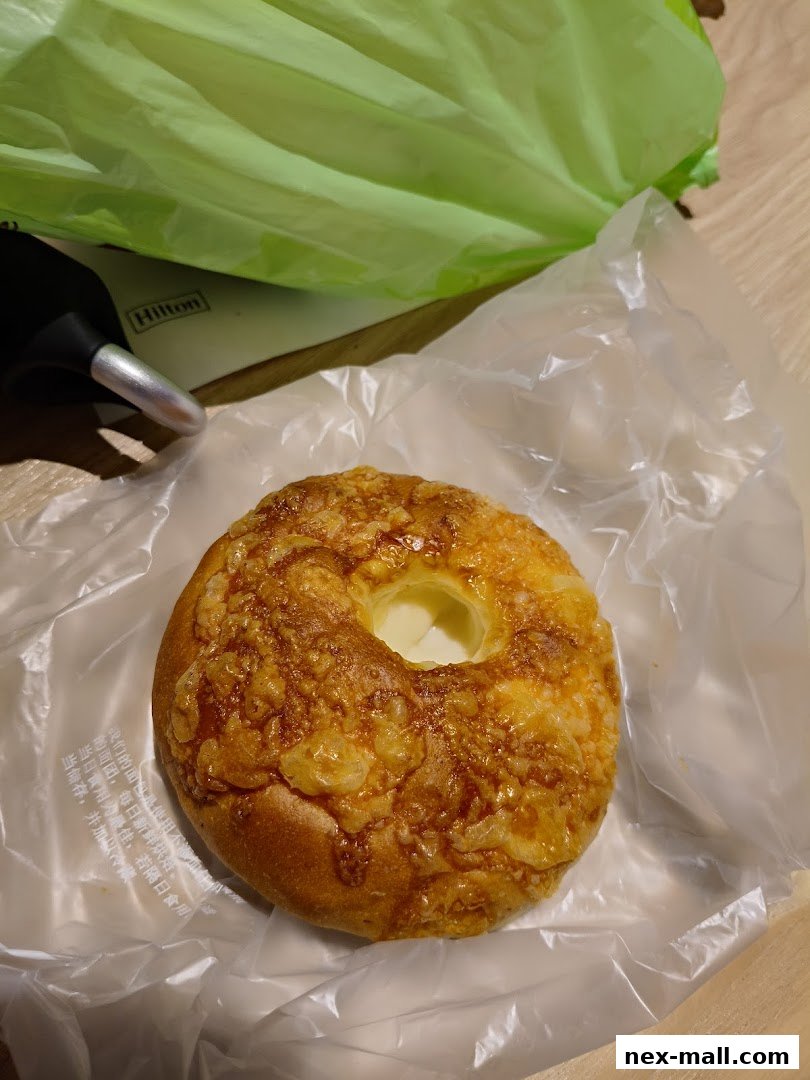 A close-up of a cheese-covered bun with a hole in the center, wrapped in plastic.