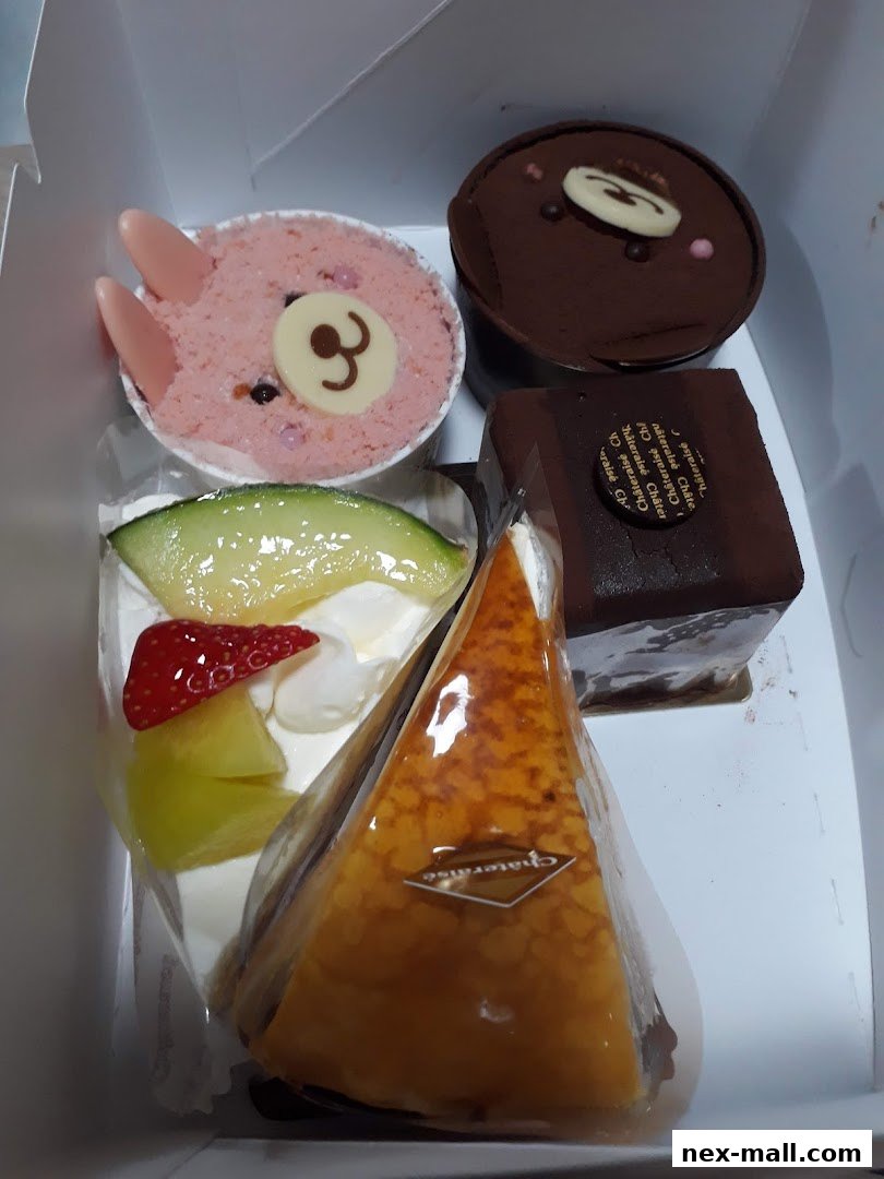 A box filled with assorted Châteraisé cakes, including a bear-faced dessert and fruit-topped slices.