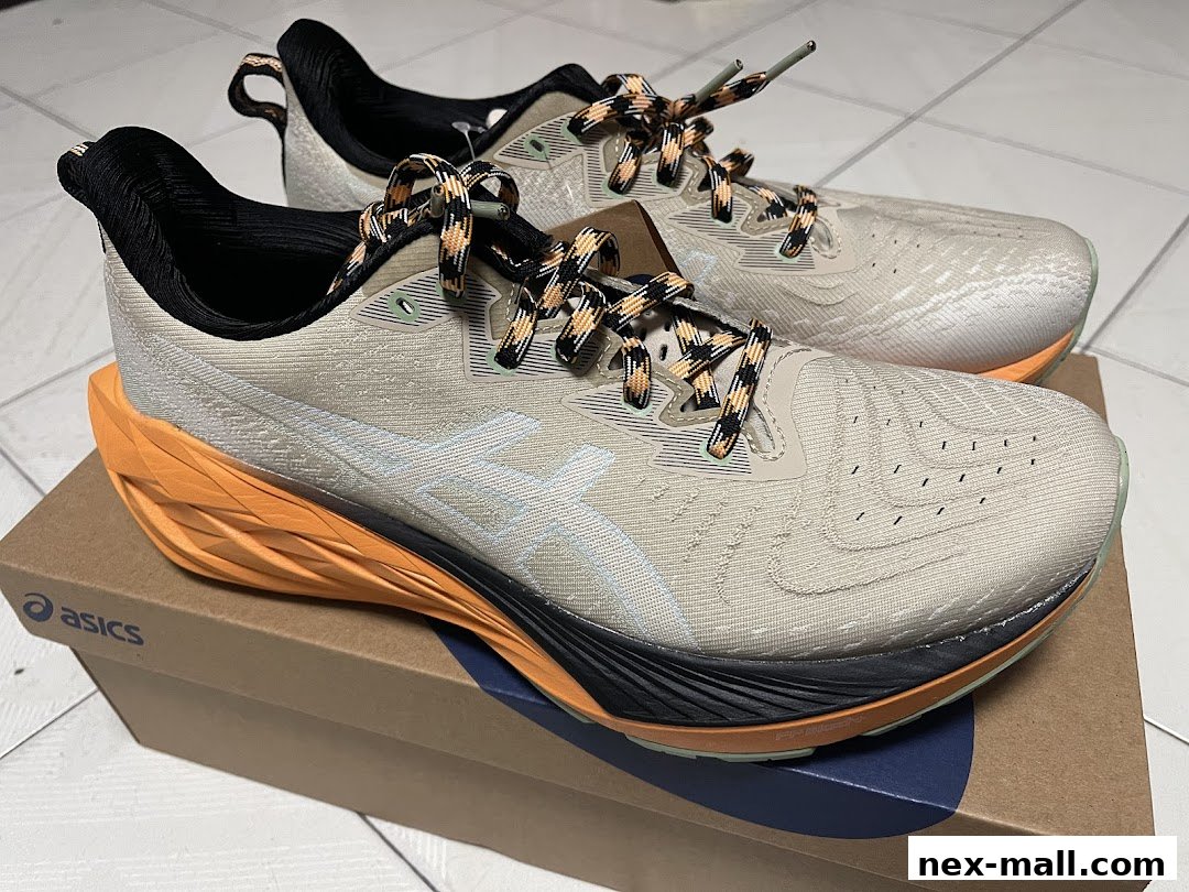 A pair of beige ASICS running shoes with orange and black accents on a shoebox.