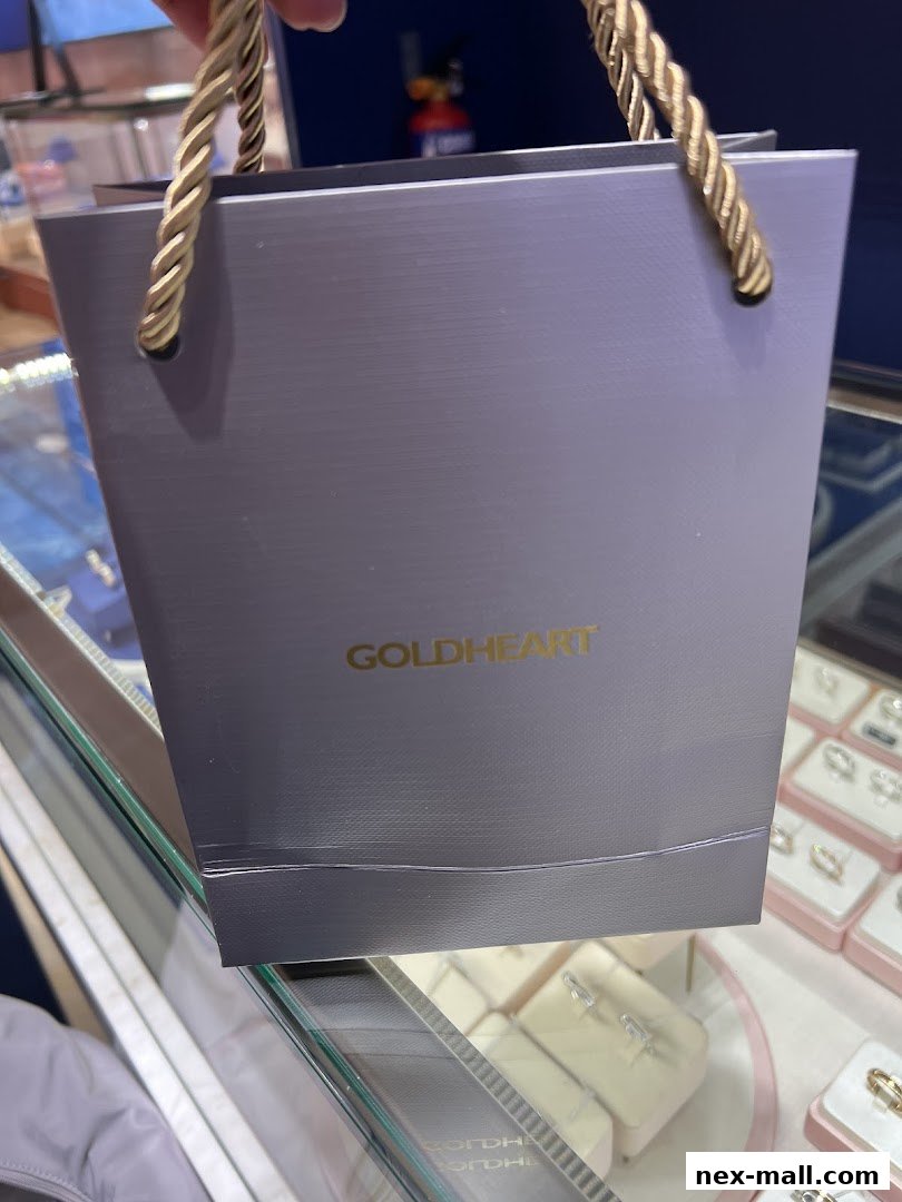 A person holds a grey shopping bag with 'GOLDHEART' logo in front of a jewelry display.