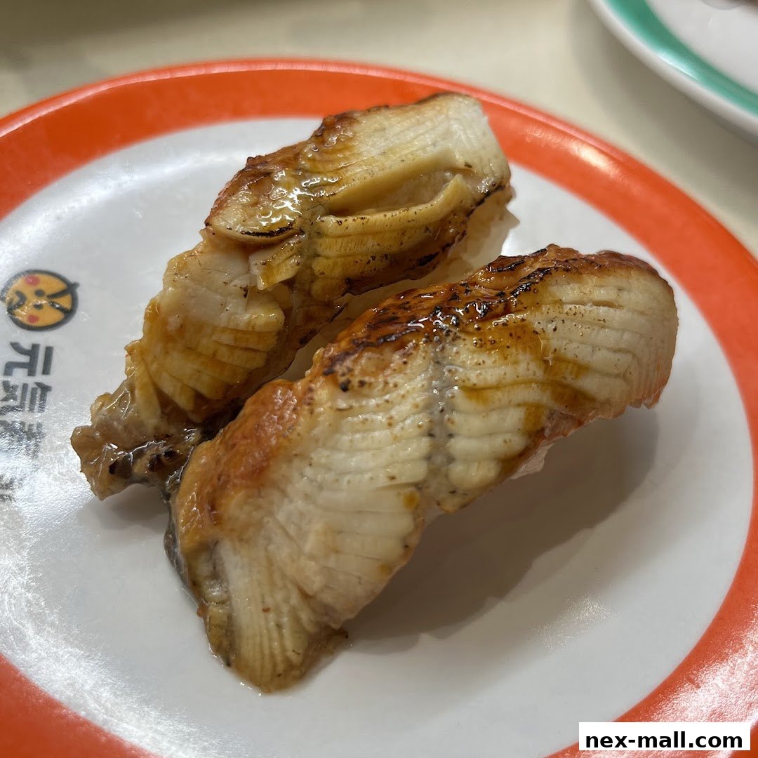 Two pieces of grilled eel sushi on a white plate with an orange rim.