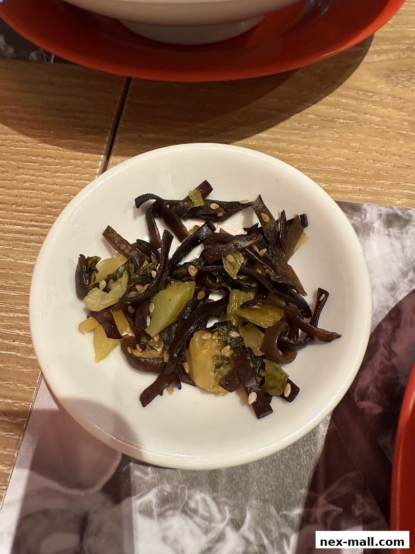 A small white bowl filled with a Japanese appetizer, possibly pickled vegetables and seaweed.