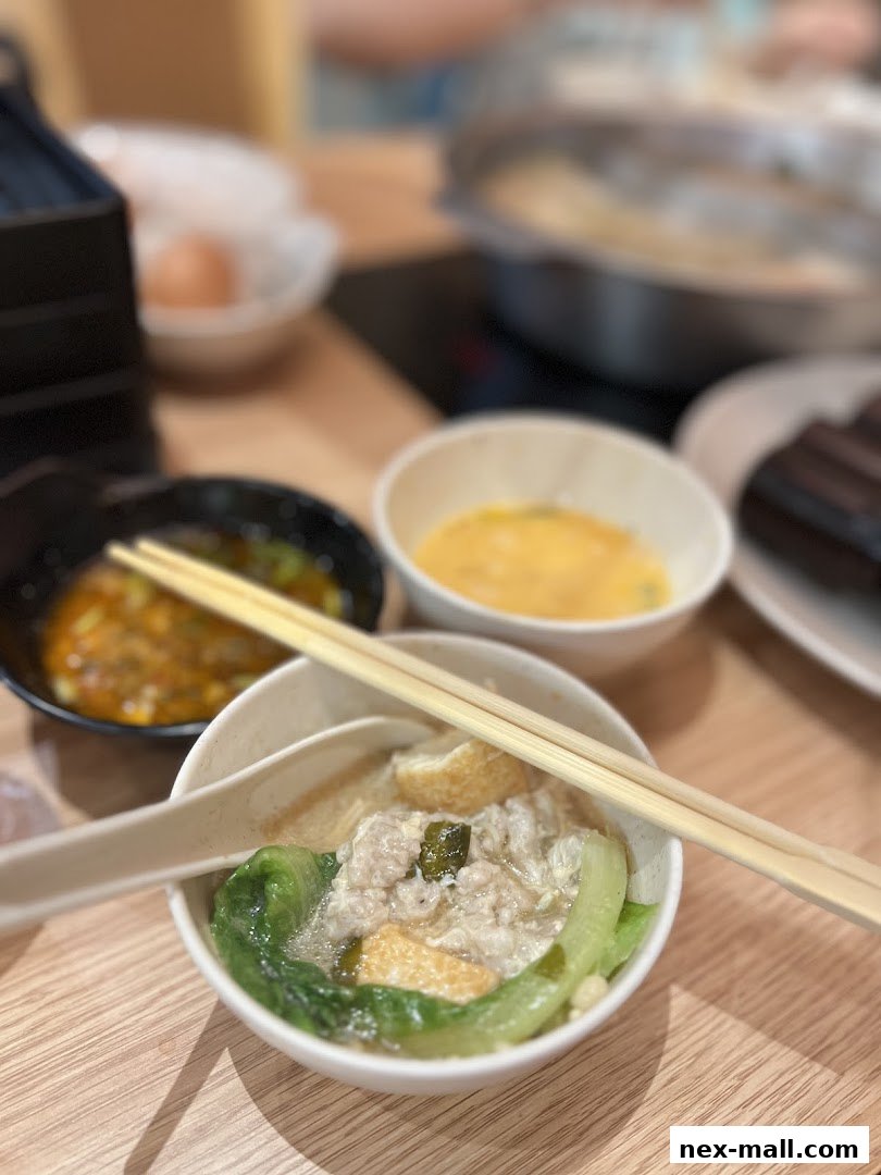 A close-up of a shabu-shabu bowl with meat, vegetables, and tofu, accompanied by dipping sauce and raw egg.
