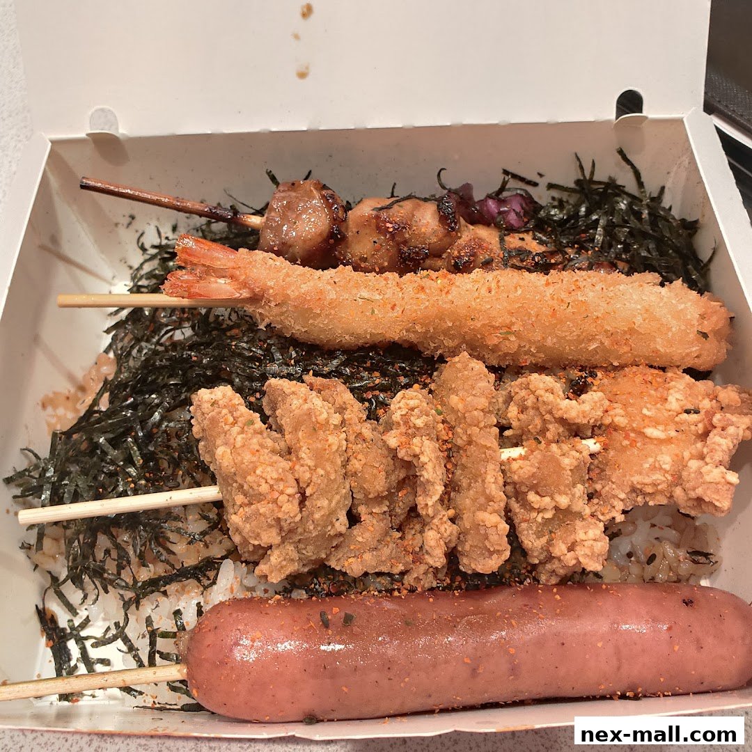 A takeout box filled with assorted grilled skewers and fried items on rice.