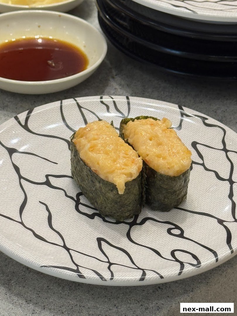 Two pieces of sushi with creamy topping on a patterned plate with soy sauce.