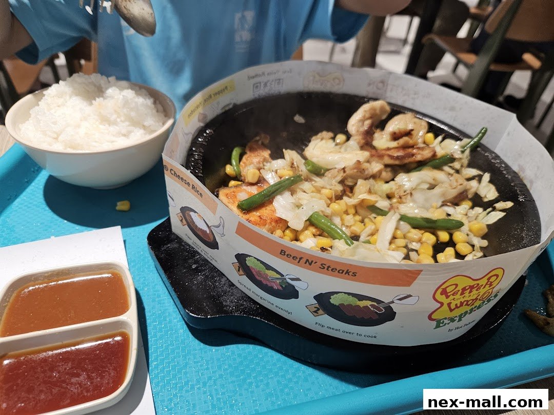 A sizzling hot plate meal with beef, corn, cabbage, and green beans, served with rice and sauces.