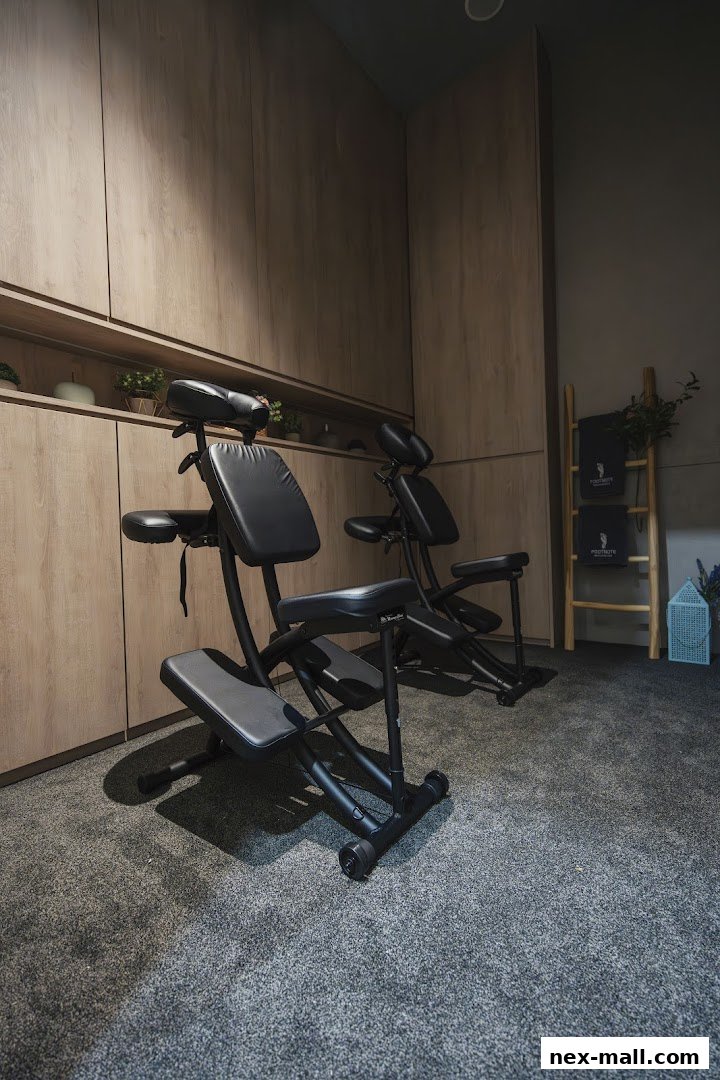 Two black massage chairs are set up in a room with wooden paneling and carpeted floor.
