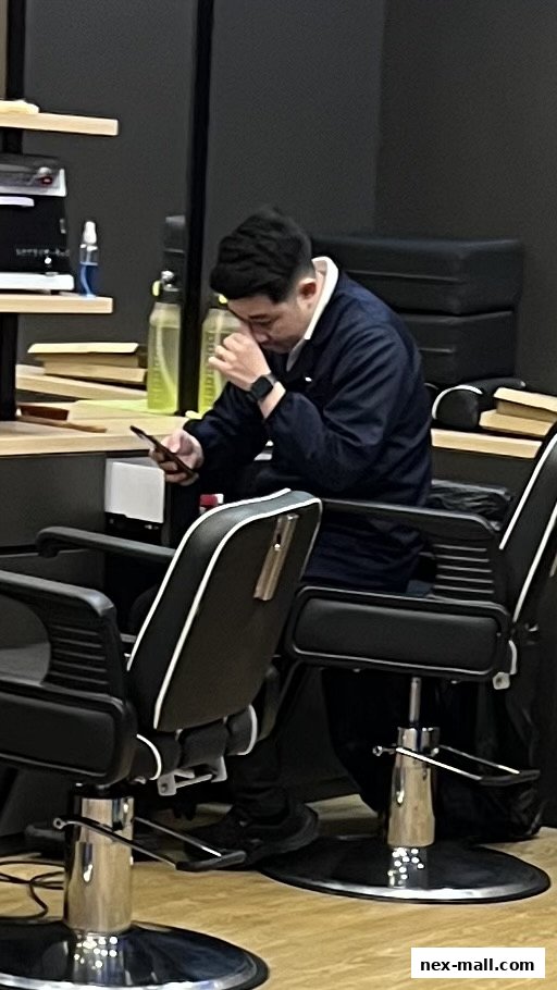 A man sits in a barber chair, looking at his phone.