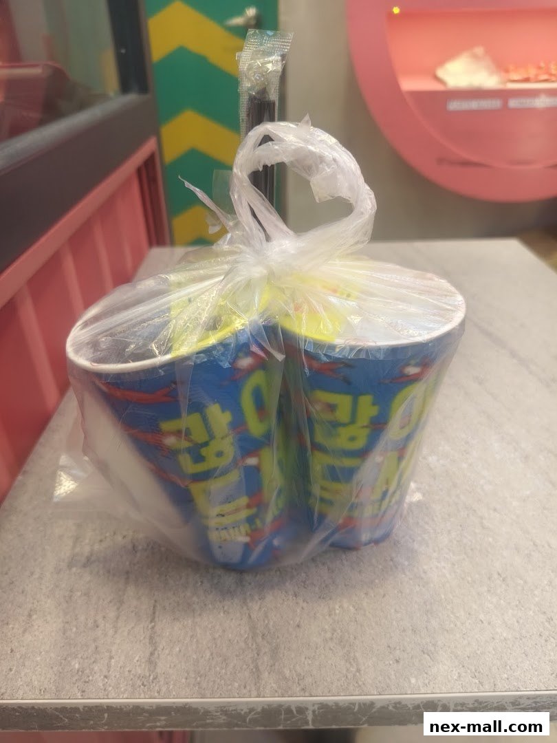 Two cups of JINJJA Chicken packaged in a plastic bag with cutlery.