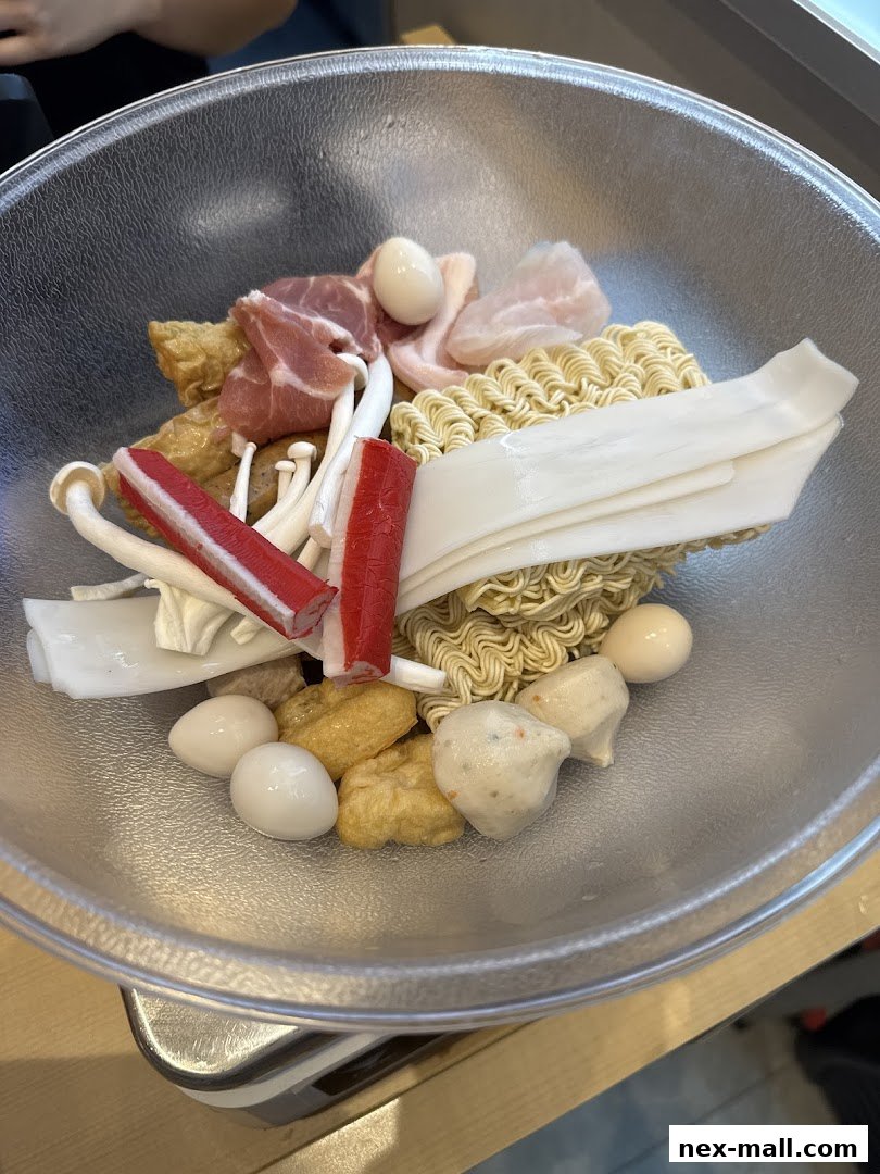 A clear bowl filled with various ingredients for Mala Tang, including noodles, meats, and seafood.