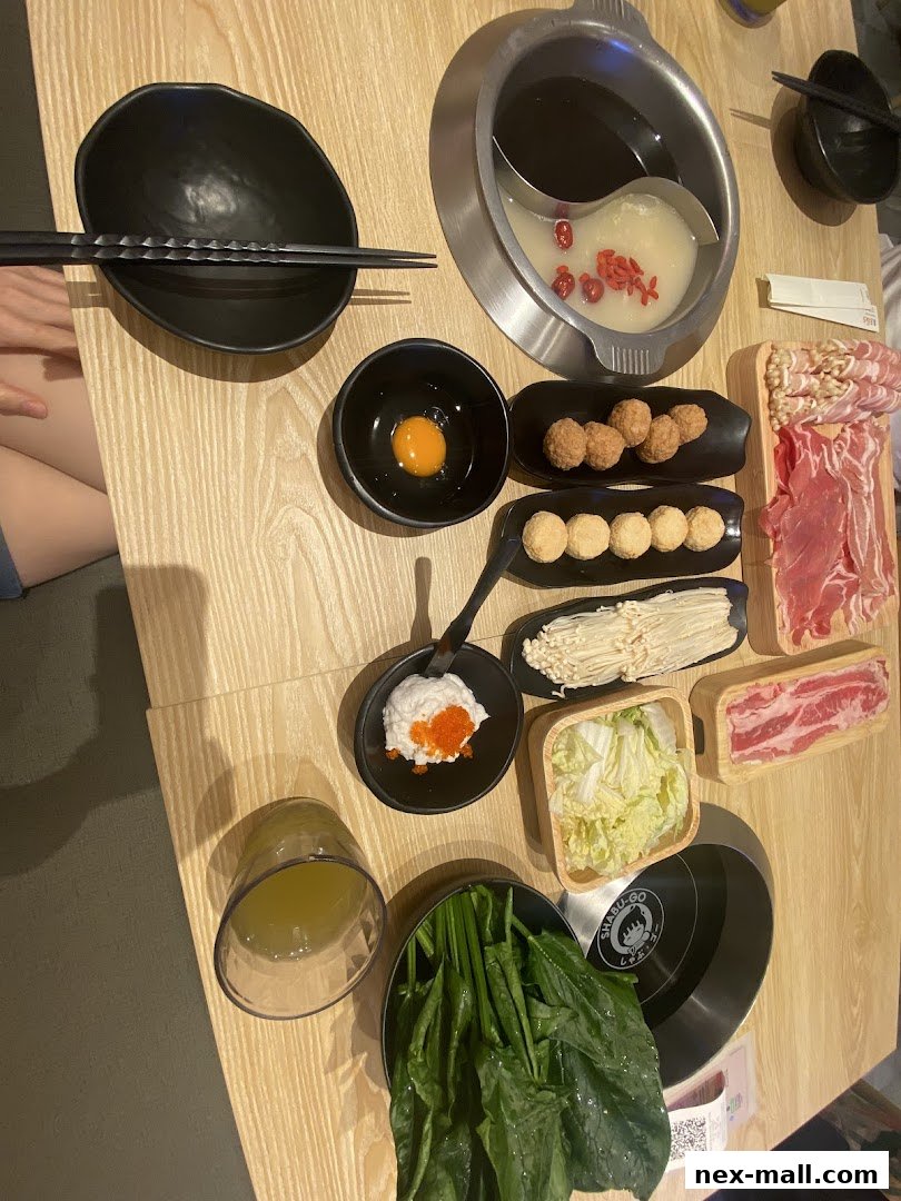 A table laden with ingredients for a hot pot meal, including meats, vegetables, and dipping sauces.