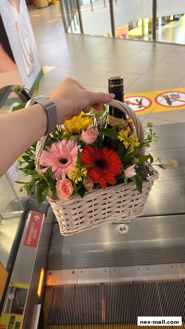 A hand holds a flower basket with a bottle of wine on an escalator.