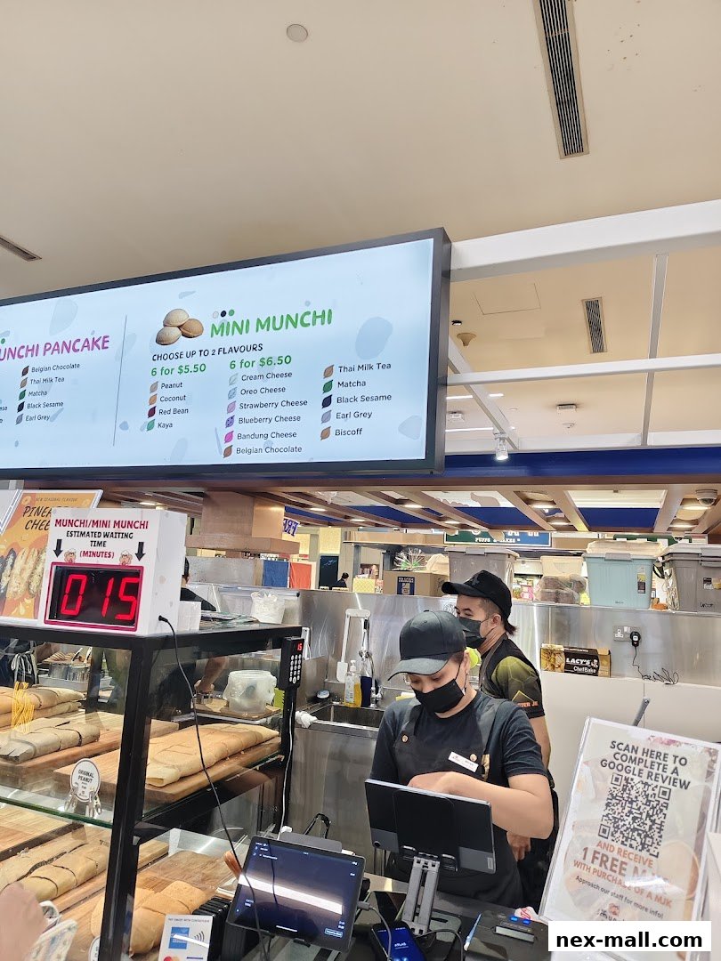 Staff serving customers at Munchi Pancakes with a menu board and waiting time display.